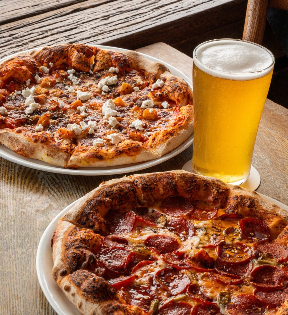 Two pizzas and a pint of beer on a waterfront table at The Dock Mooloolaba. $20 Pizza & a Pint State of Origin Special